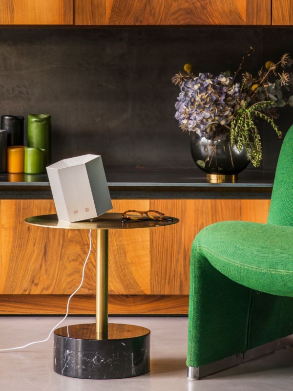 Purificateur d'air compact de Shield by JVD posé sur une table à côté d'un fauteuil vert