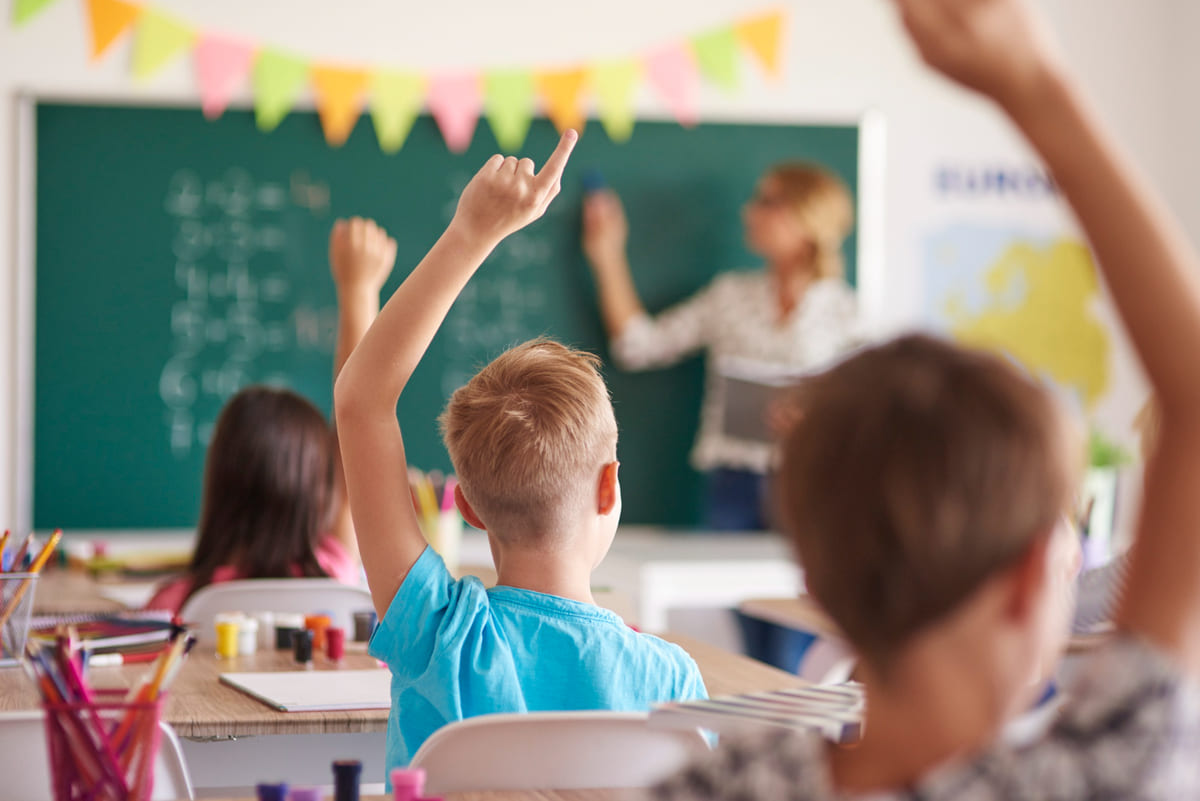 des élèves de primaires qui lèvent la main dans une salle de classe