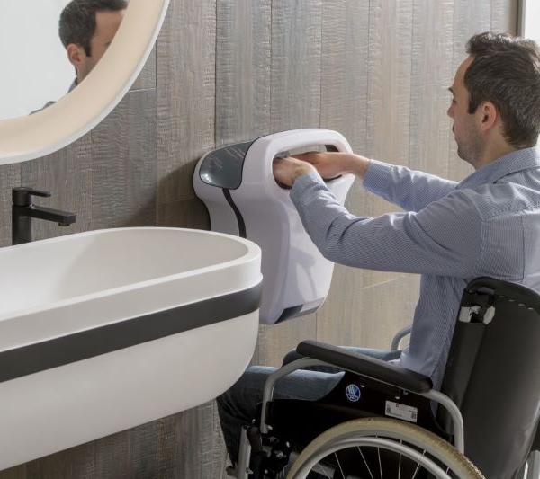 personne en fauteuil roulant qui se sèche les mains avec un sèche-mains JVD adapté