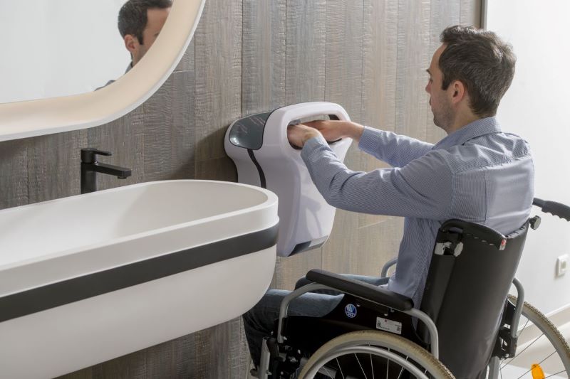 personne en fauteuil roulant qui se sèche les mains avec un sèche-mains JVD adapté